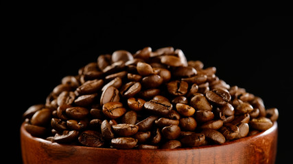 roasted coffee beans in wooden bowl. black background macro shot