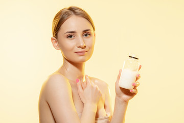 Close up of beautiful young woman massaging skin with moisturizer yellow background. Concept of cosmetics, makeup, natural and eco treatment, skin care. Shiny and healthy skin, fashion, healthcare.