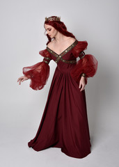 Portrait of a beautiful woman with red hair wearing  a  flowing Burgundy fantasy gown and golden...