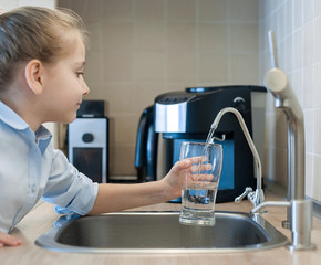 Child pouring fresh reverse osmosis purified water in kitchen at home. Drinking tap water....