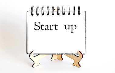 Desk with stationary and notebook with text Start up.