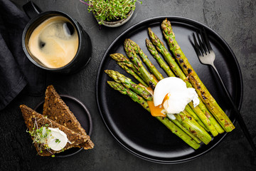 Roasted asparagus with poached egg on plate on black background, top view