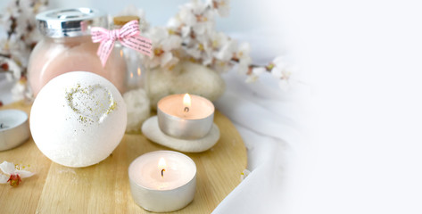Obraz na płótnie Canvas Romantic spa with bath bomb, cosmetic scrub, candles and cherry blossom. Still life skincare products. Resort concept for Valentines day, Mothers day or wedding greeting card.