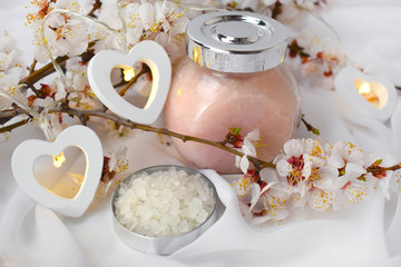 Close up aromatherapy spa composition with cosmetic scrub, sea salt, heart lights and cherry blossom. Resort concept for Valentines day, Mothers day or wedding greeting card.