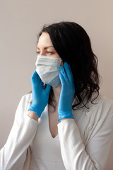 A woman in gloves and a protective mask stands on a light background in a white jacket. The concept of suppression of coronavirus