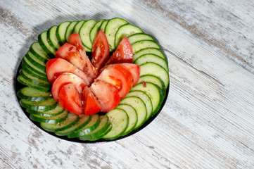 chopped cucumbers and tomatoes in a black plate on a light wood background