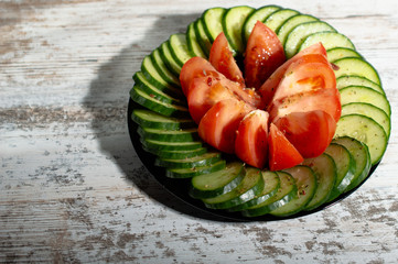 chopped cucumbers and tomatoes in a black plate on a light wood background