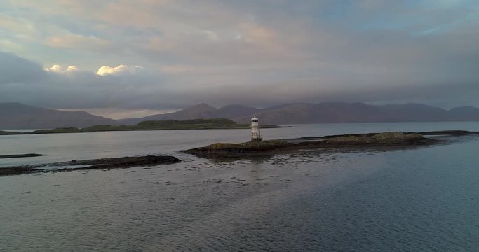 Lighthouse on rocky outcrop with surrounding mountains and islands. Scotland, UK