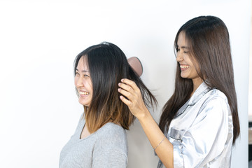 Photo of joyful Asian girl drying her friend's hair and having fun.