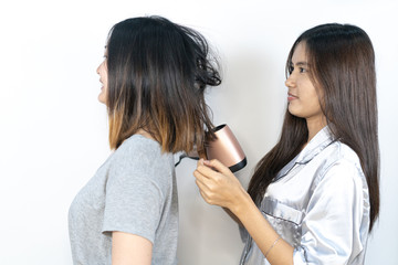 Photo of joyful Asian girl drying her friend's hair and having fun.