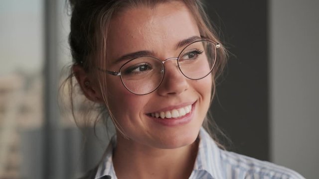 A close-up view of a happy young woman wearing glasses is looking and posing to the camera at home  
