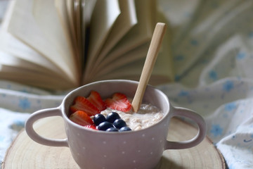 Bowl of porridge with fruit toppings and open book in bed. Selective focus.
