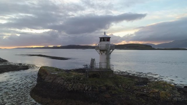 Old lighthouse at sunset overlooking mountains and islands