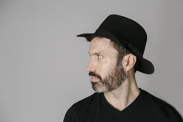 Profile portrait of a handsome bearded middle-aged man with hat against neutral background