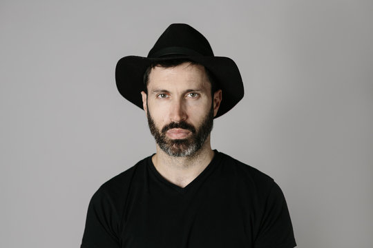 Close-up portrait of a handsome bearded middle-aged man with hat against neutral background