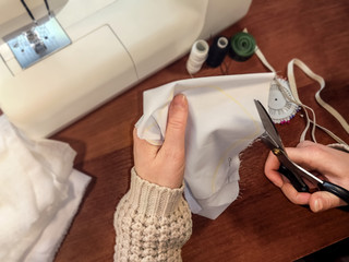 Girl seamstress cuts out a pattern of white fabric with scissors, top view, close-up. Beautiful sewing background with copy space, work stage, atelier or handmade services