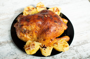 fried chicken with potatoes on a black plate on a white wooden background