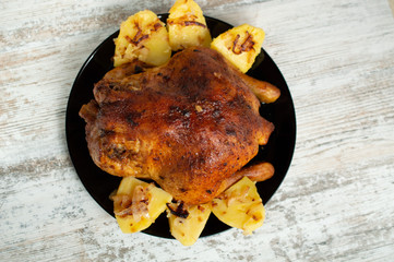 fried chicken with potatoes on a black plate on a white wooden background