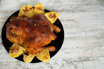 fried chicken with potatoes on a black plate on a white wooden background