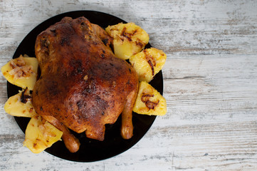 fried chicken with potatoes on a black plate on a white wooden background