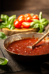 Classic homemade Italian tomato sauce with basil for pasta and pizza in the pan on wooden background.