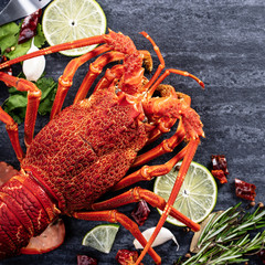 Cooked boiled lobster, delicious dinner seafood meal set with knife and fork on black stone slate background, restaurant menu design, top view, overhead