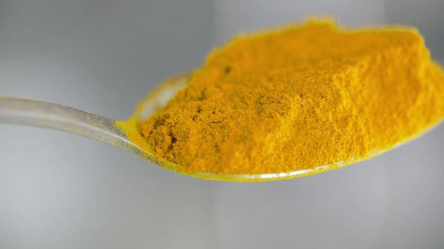 Turmeric powder on tea spoon. Shot extreme close up with professional macro lens. camera pans slowly from left to right. Pro res 4K