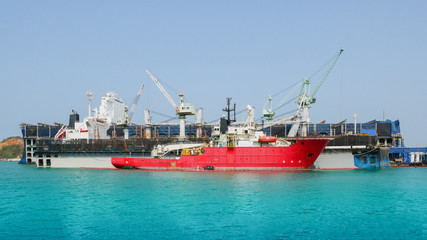 Naklejka premium Tugboat mooring at beside floating dry dock in shipyard during cargo ship repair and crane work lifting in floating dock background.