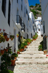Fototapeta na wymiar A view of a narrow, steep alley in the amiable, pretty small white town of Frigiliana, in Andalusia, southern Spain. Picturesque scenery with beautiful flowers decorating the setting.