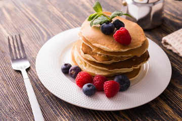 Pancakes with blueberries and raspberry on wooden background. Breakfast and traditional meal.