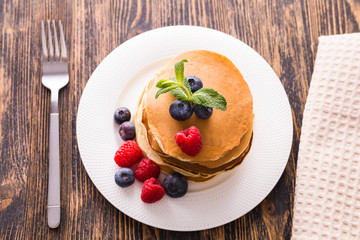 Homemade sweet pancakes with blueberries and raspberries on a white plate, top view.