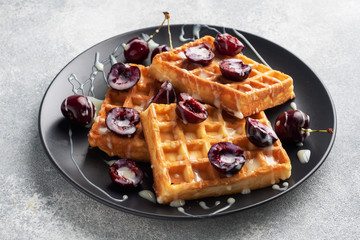 Belgian fluted waffles with fresh cherries and cream on a plate. Soft homemade waffles, sweet dessert with cherries.