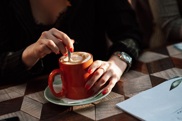 Girl in a cafe with a mug of hot drink. Close-up of hands and mug with cappuchino, lifestyle