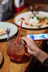 girl holds a glass with  a summer refreshing cocktail on a wooden table background in a restaurant. Close-up of a hand. Cocktail decorated with a sprig of lavender