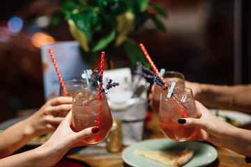 Girls in a restaurant clink glasses with a fresh summer cocktail. close-up of hands and glasses. Many Hands toasting with glasses