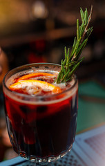 A glass of a warming red wine drink decorated with a  rosemary and citrus