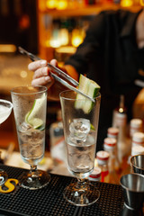 Bartender decorates cocktail with cucumber slice using tweezers.  Close-up on hands