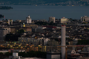 Zurich city Switzerland view with tall concrete illuminated chimney from famous vista point in the evening blue hour evening after sunset cloudy sky