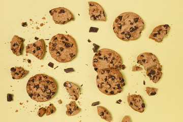 Top view of a baked chocolate broken and whole cookies with peace of pure chocolate and yellow background 