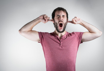 Young beard man with a grimace of suffering, screaming while covering his ears. Mental health, stress and anxiety mood. On a white background.
