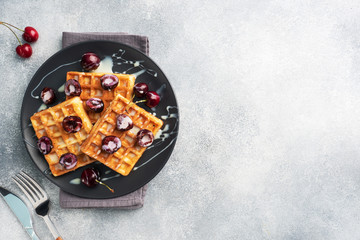 Belgian fluted waffles with fresh cherries and cream on a plate. Soft homemade waffles, sweet dessert with cherries. copy space
