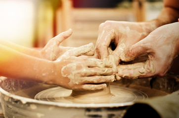 Master teaches child to make a ceramic pot by molding clay on throwing wheel. Close up hands of the...