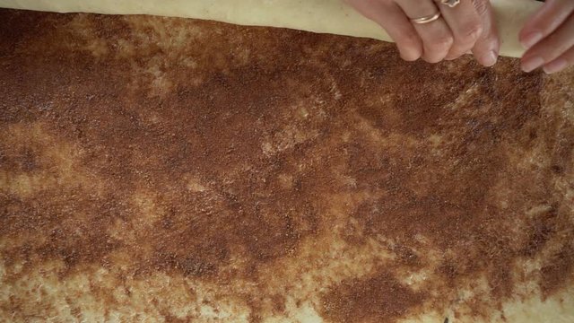 A young woman cook pastry chef rolls a roll of raw cinnamon dough to make cinnabon buns. Slow motion.