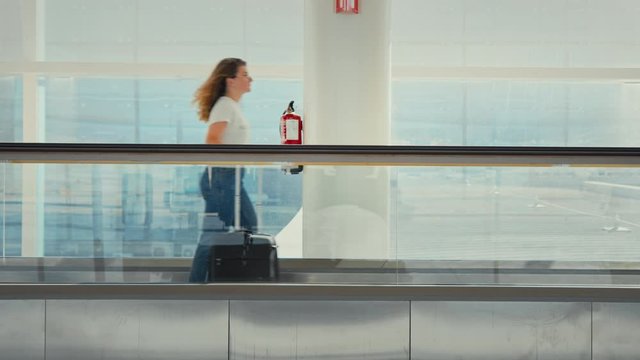 Female solo traveller walks fast on moving walkway or travelator. Woman walk to gate through terminal in airport. Travelling to home country to destination, in empty terminal 