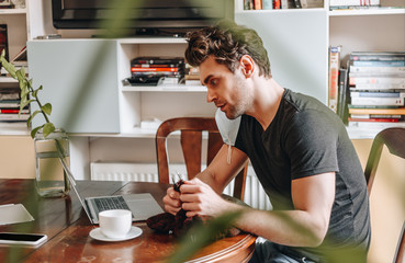 side view of concentrated young man looking at laptop while knitting at home
