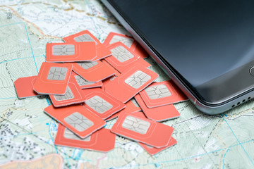 many sim cards and a mobile phone are at the top of the geographical map. Travel concept of traveling around the world with the change of different mobile providers.