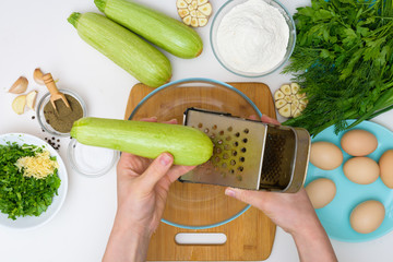 step by step recipe to cook zucchini pancakes and greens on a light background on a wooden Board . recipe with the addition of eggs and flour, garlic, pepper. the view from the top. grate the zucchini