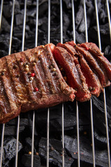 cut fresh grilled tasty steak with rare roasting and condiments on grate above black coals