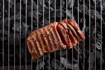 top view of cut fresh grilled tasty steak with rare roasting on grate above black coals