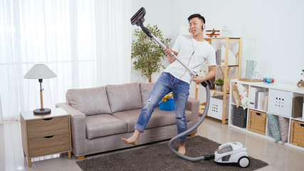 household cleaning fun young man sweeping floor with earphone is listening and singing with rock...